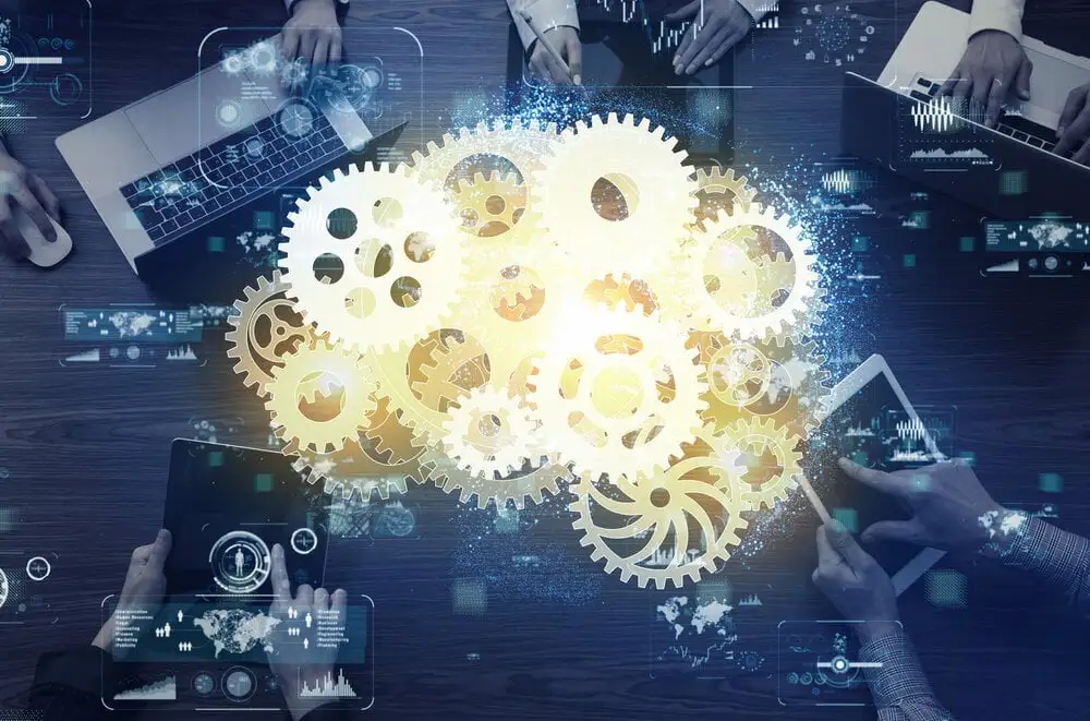 Team collaboration with laptops and tablets surrounding glowing interconnected gears, symbolizing industrial innovation and teamwork.